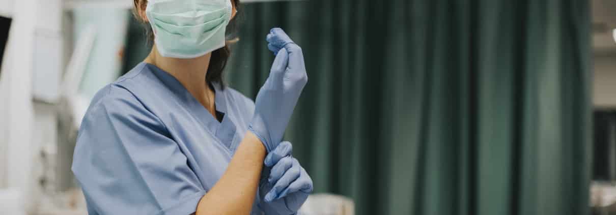 Nurse in a face mask putting on gloves