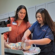 Estudiante practicando medir la cabeza de un bebé con un maniquí de simulación de bebé. Instructor mirando.