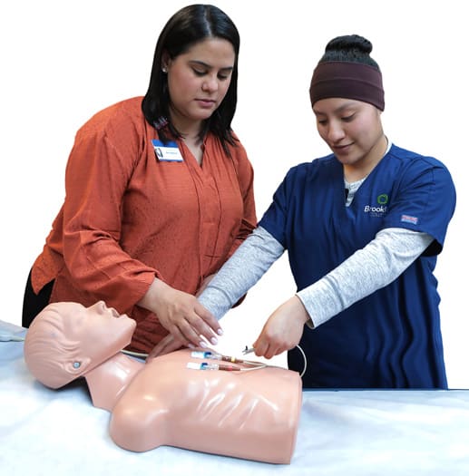 Estudiante practicando habilidades de enfermería en un maniquí con la ayuda de un instructor.
