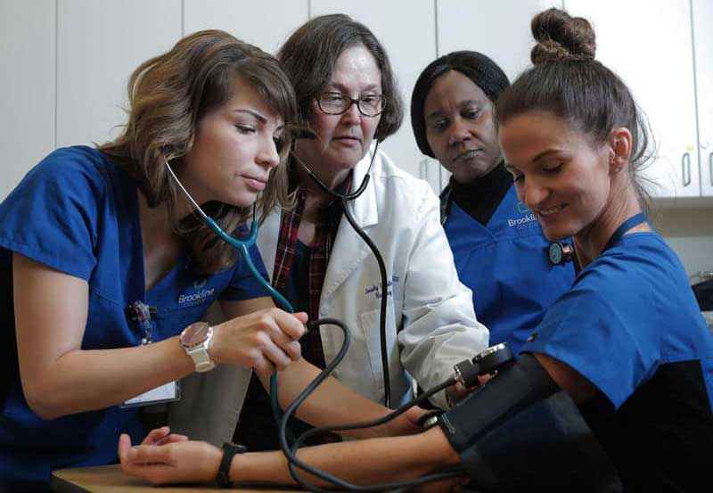 Un grupo de estudiantes de enfermería con un instructor controlando la presión arterial de otro estudiante