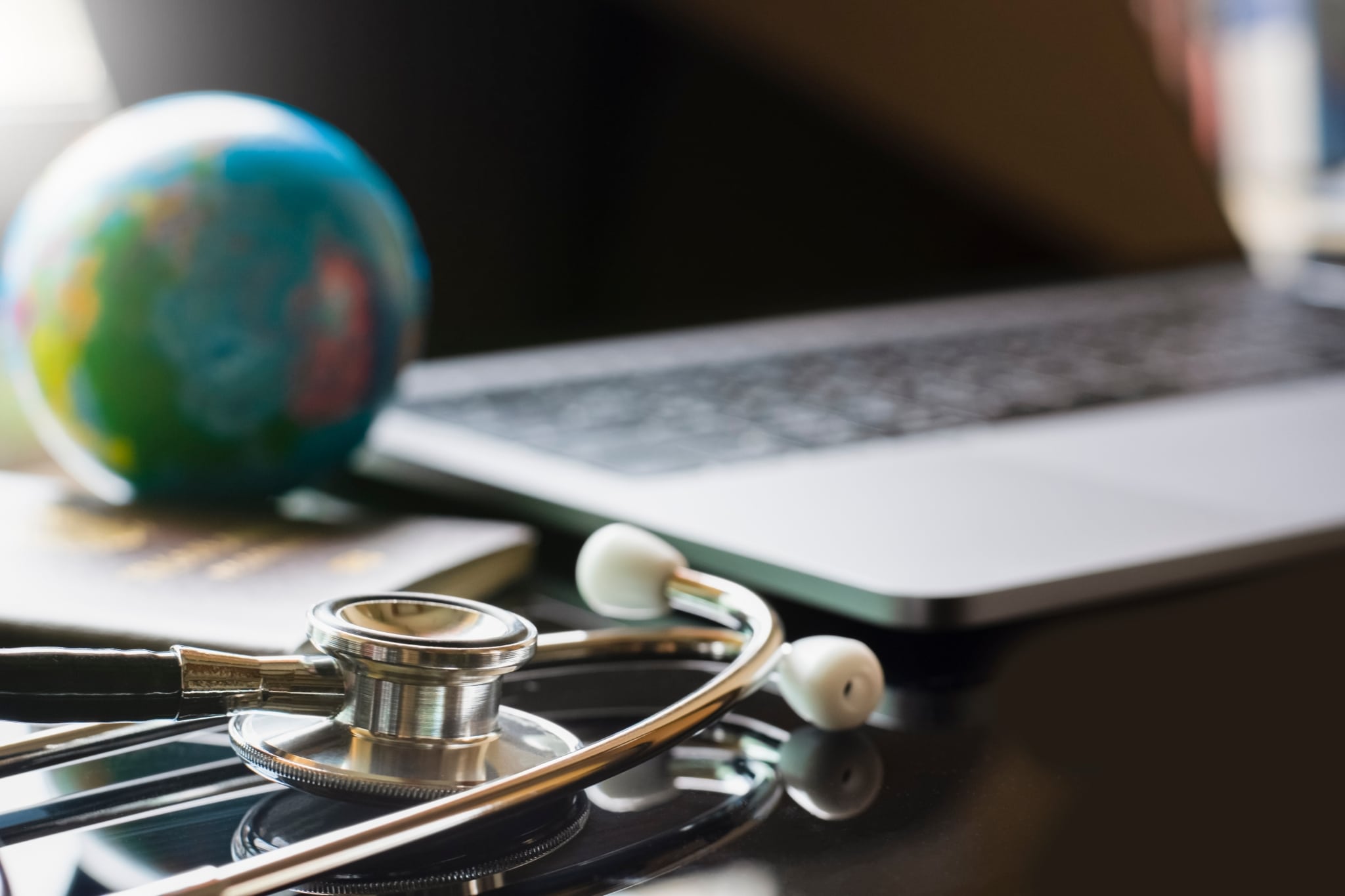 Close up of a laptop, stethoscope, and miniature globe