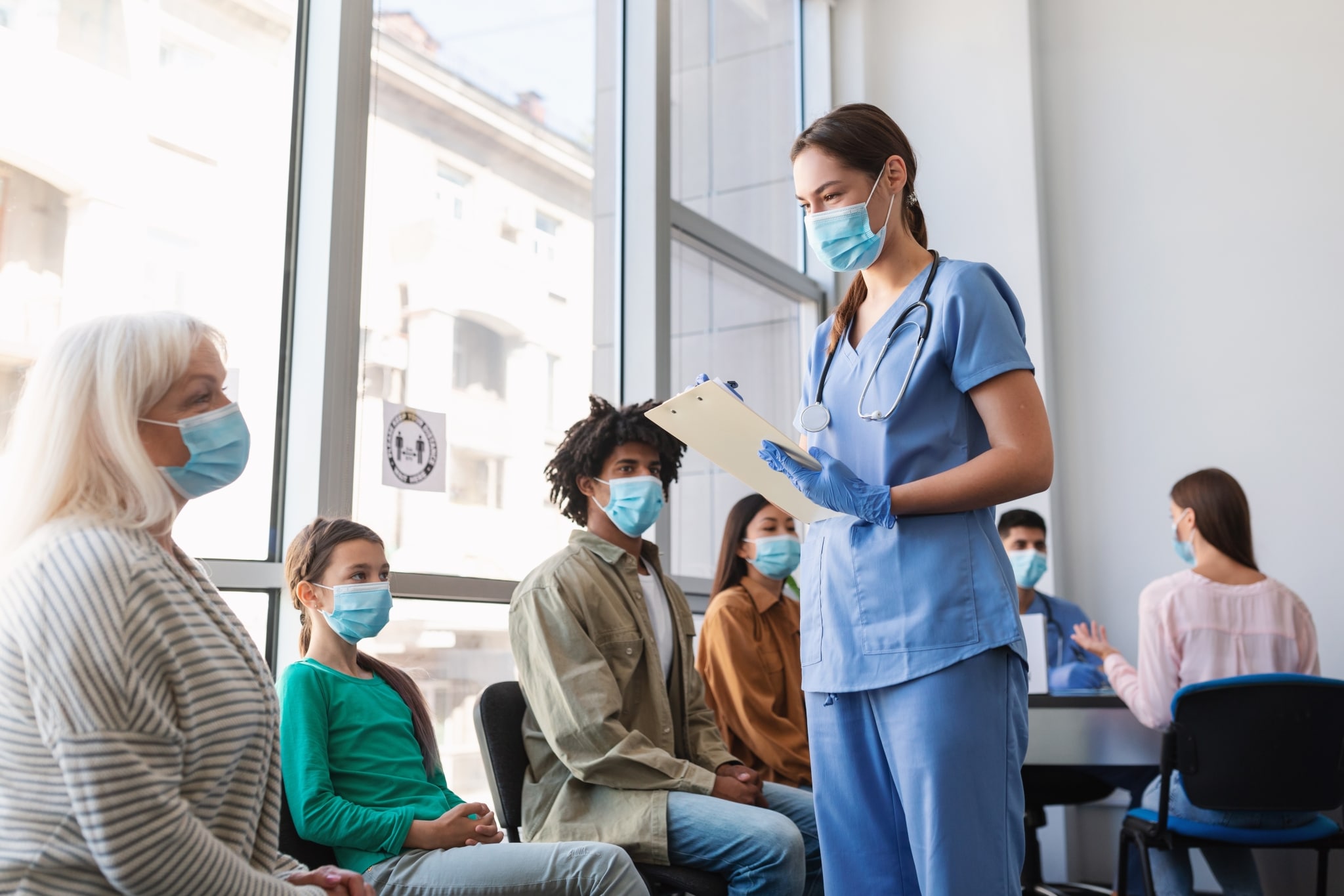Masked nurse speaking with patients in a waiting room