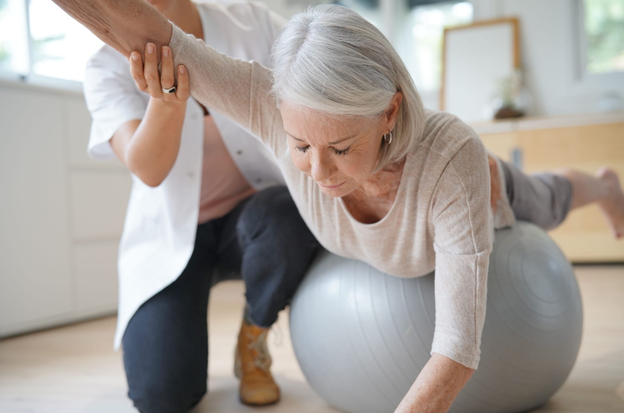 Occupational Therapist Assistant helping an elderly patient use an exercise ball