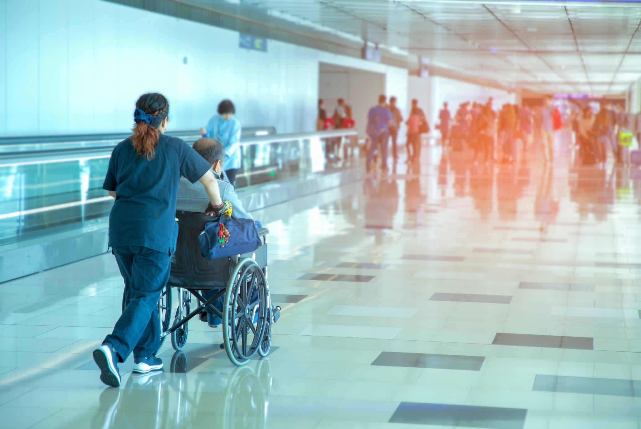 Female nurse escorting a man in a wheelchair at an airport