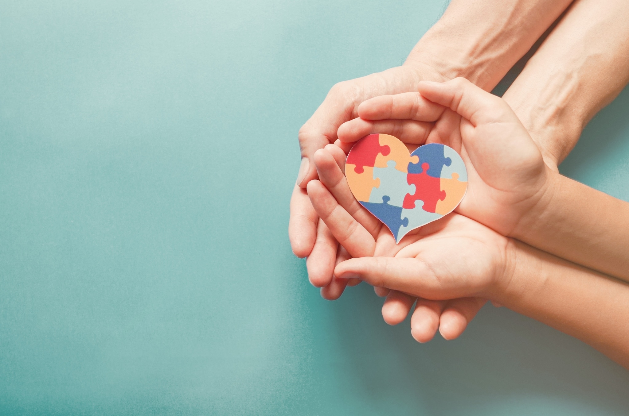 Hands holding a heart with puzzle shapes to represent autism
