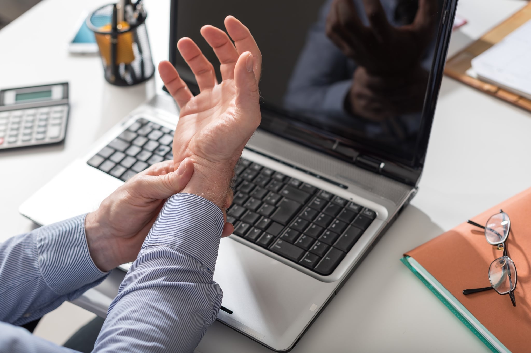 Man with carpal tunnel holding his wrist in front of a laptop