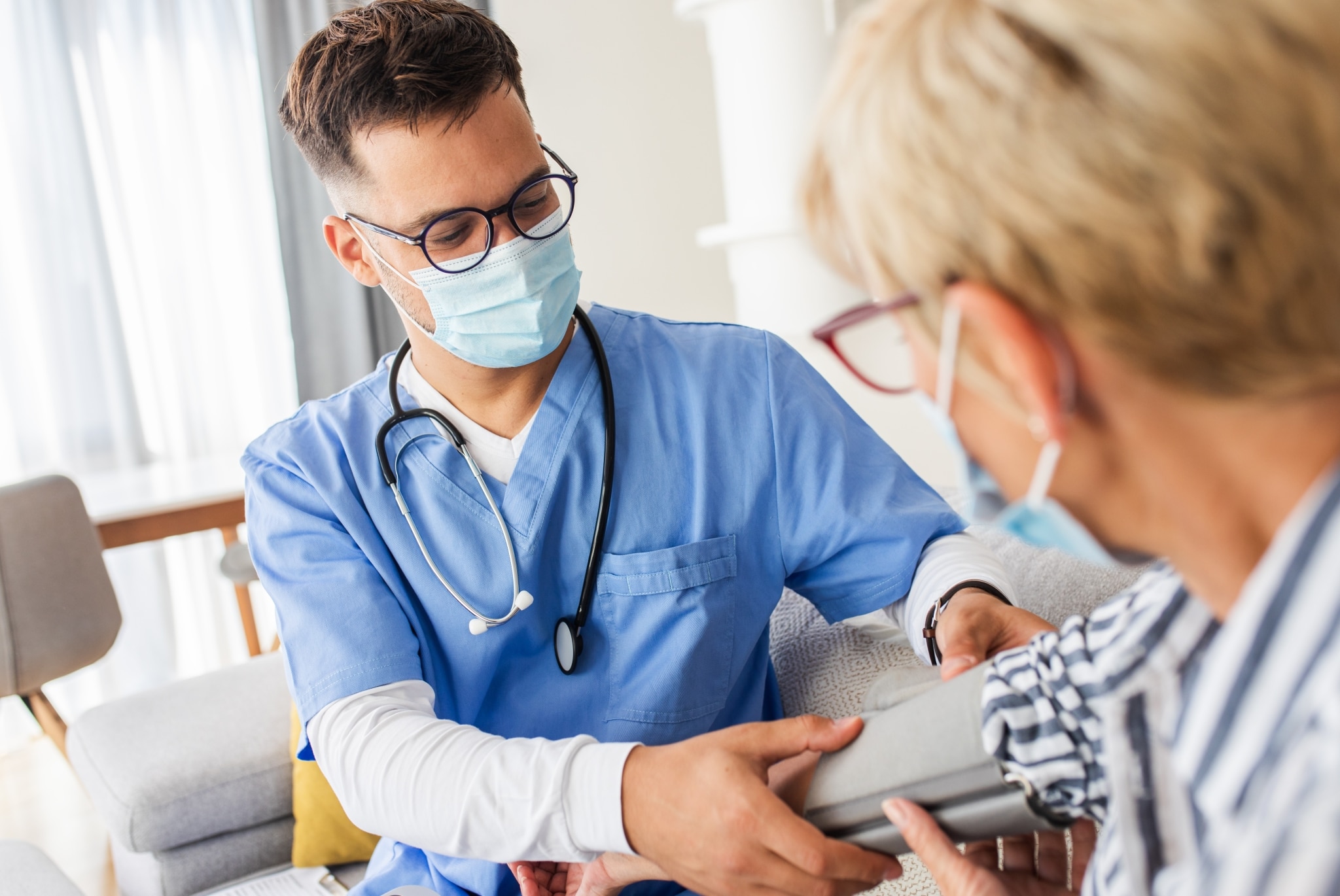 Masked male nurse taking a patient's blood pressure