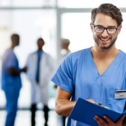 Smiling male nurse with glasses holding a patient's chart