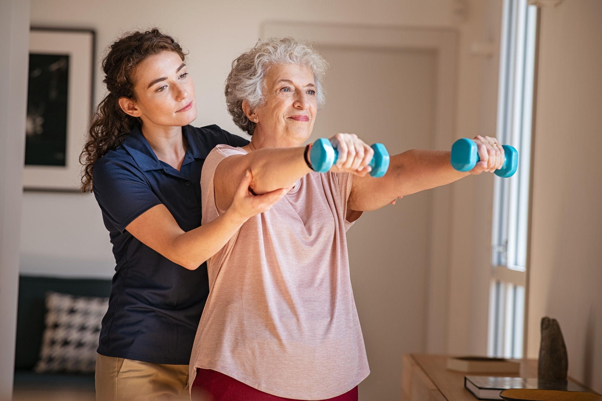 Physical therapist assistant helping an elderly woman lift weights