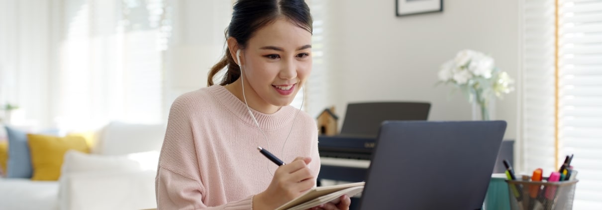 Young Asian woman uses a laptop and takes notes