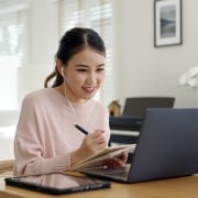 Young Asian woman uses a laptop and takes notes