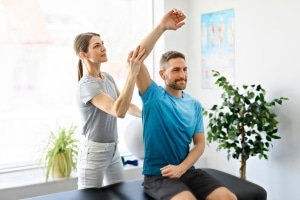Physical therapy professional helping a man stretch his arm and shoulder