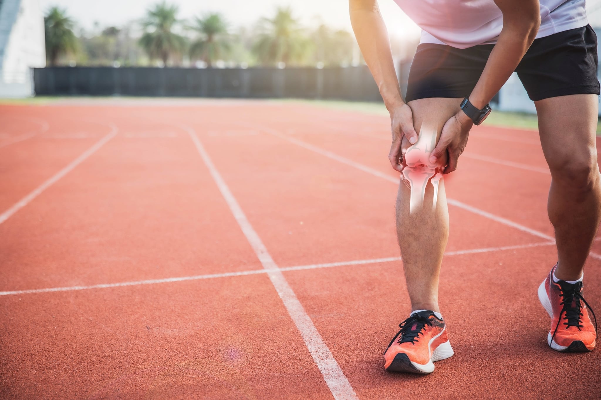 Man on a race track gripping his knee in pain
