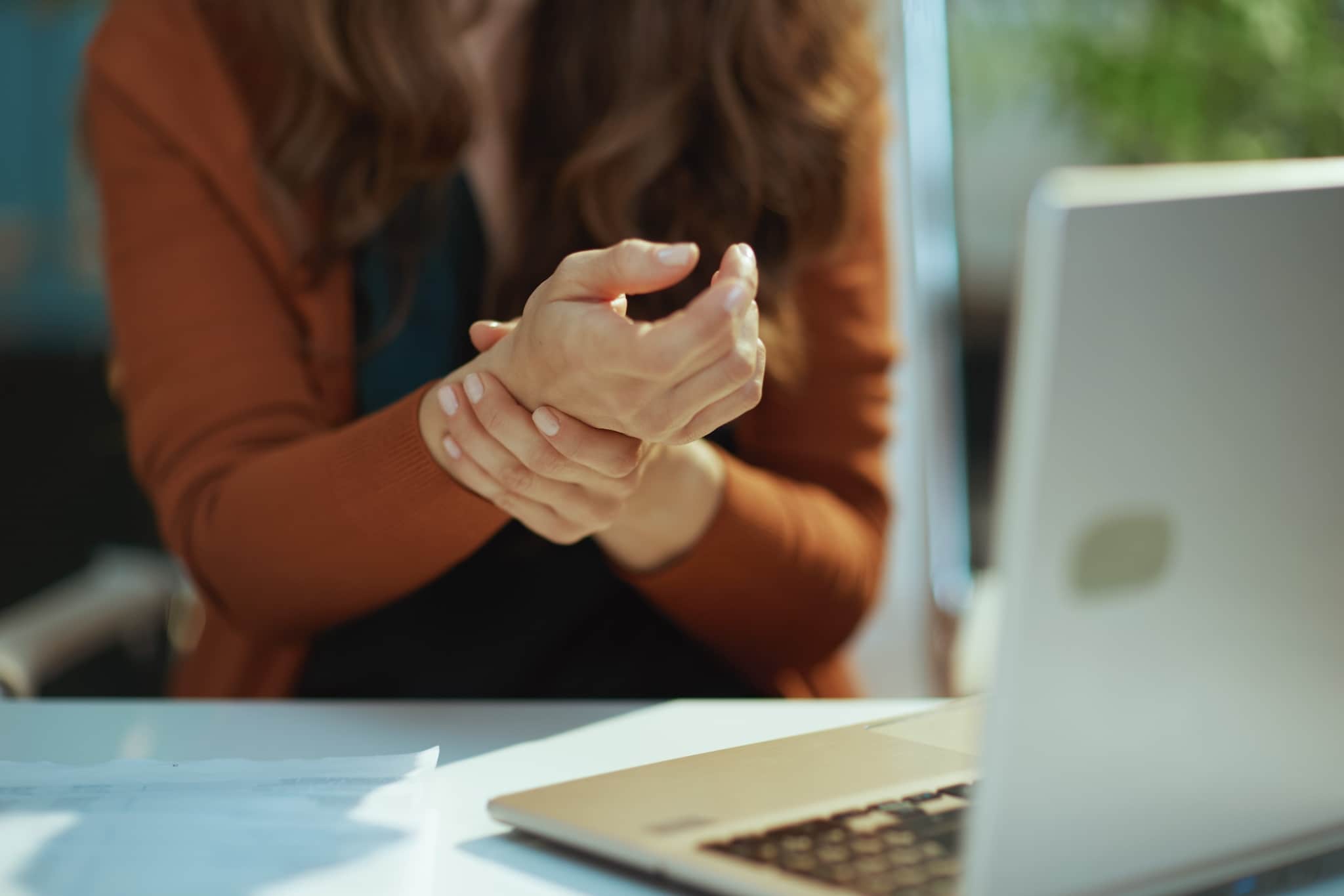 Close up of a woman at a desk holding her wrist