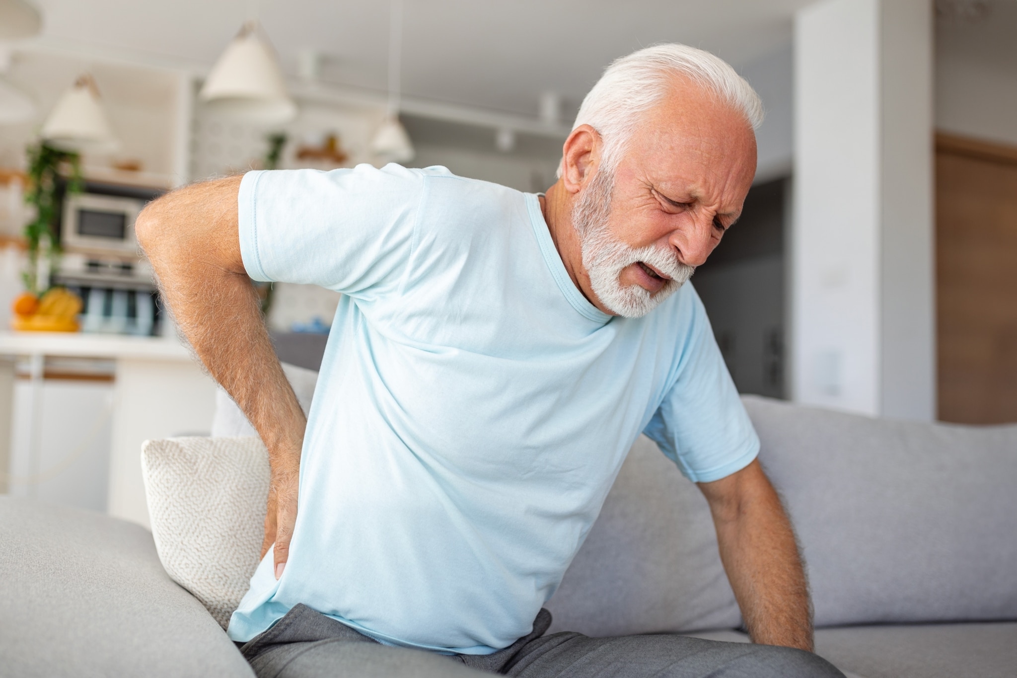 Elderly man with back pain leaning forward on a couch