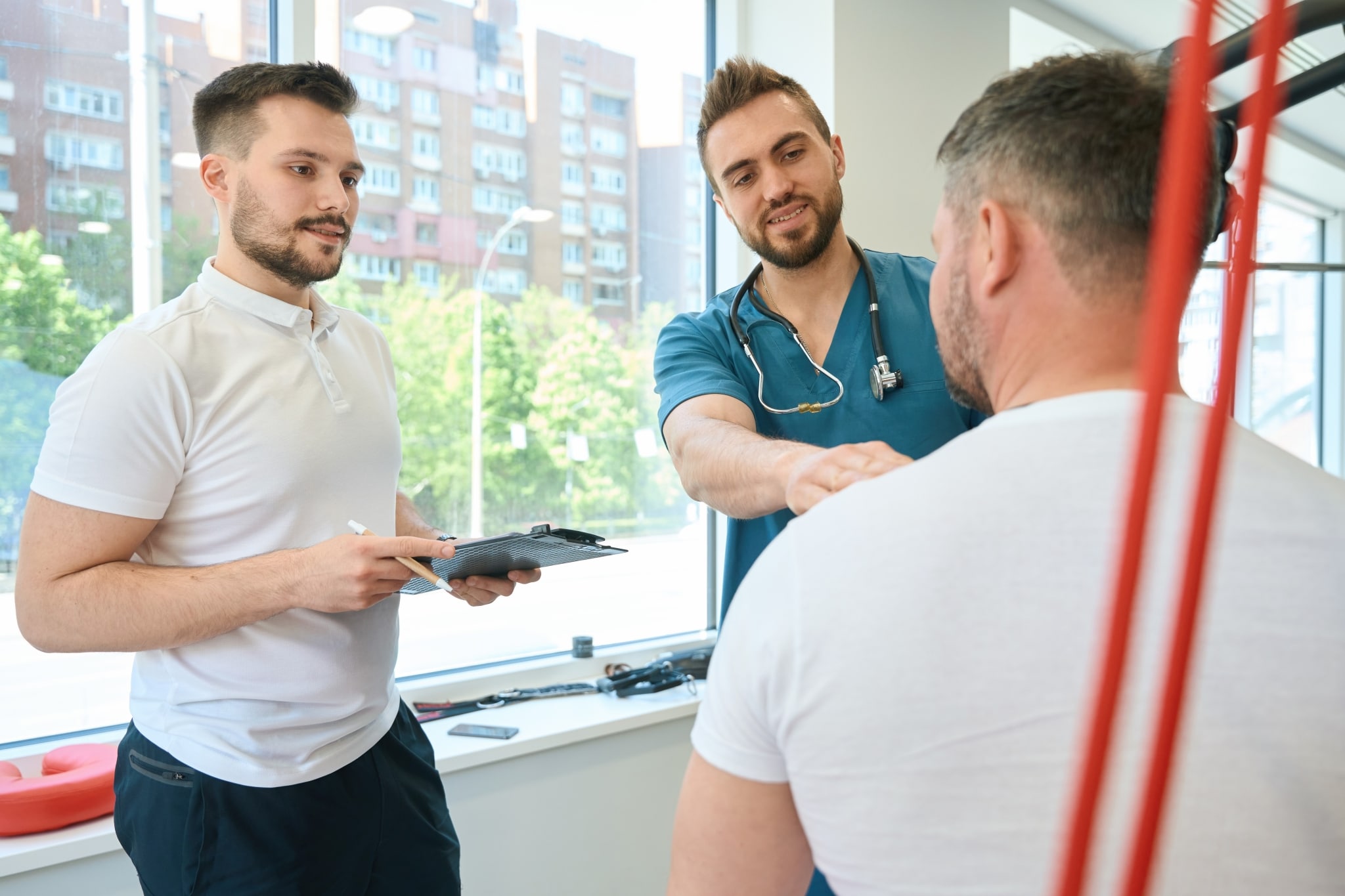 Two male fitness coaches helping a man exercise