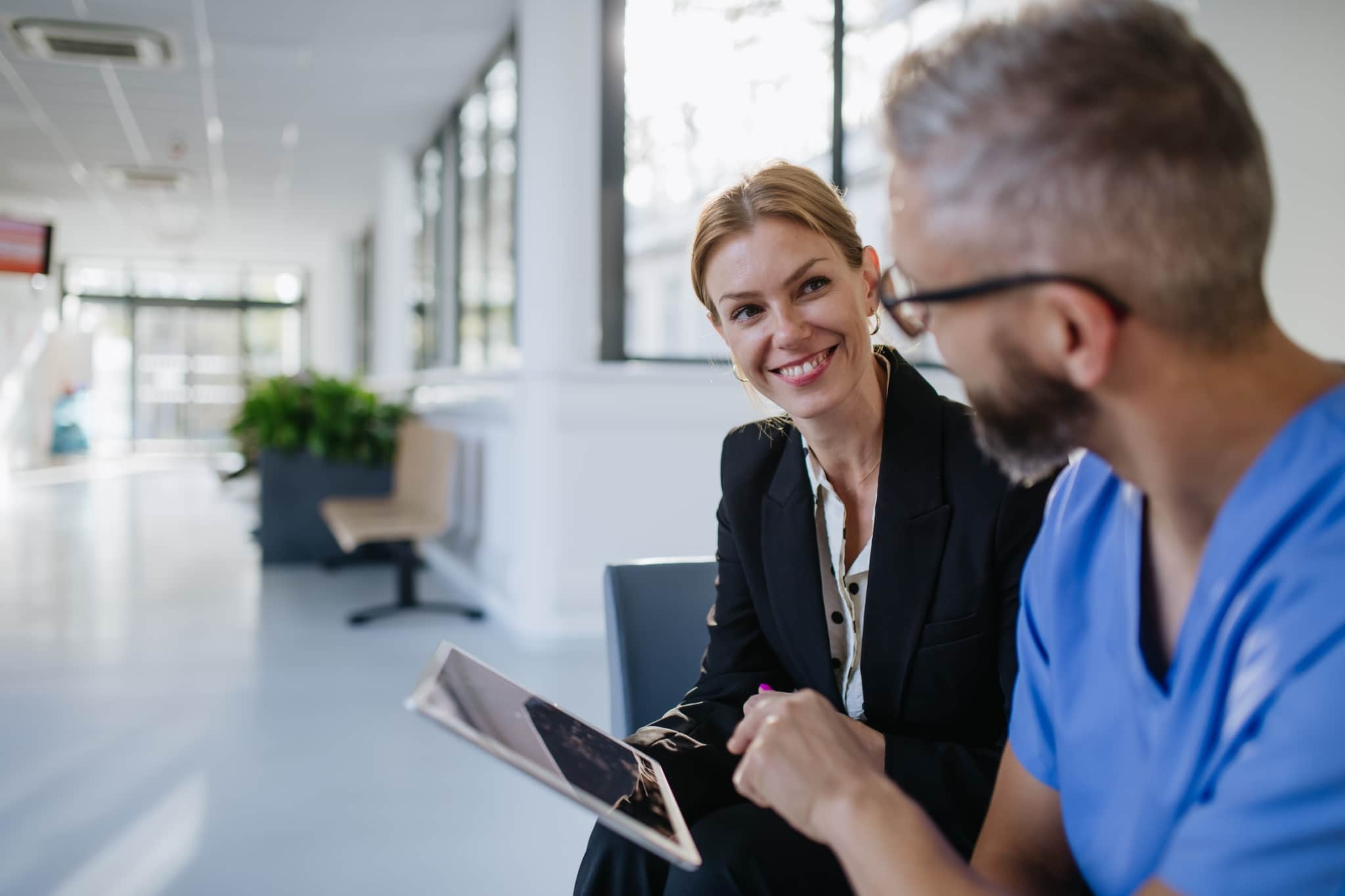 Female professional speaking with a man in scrubs and holding a tablet