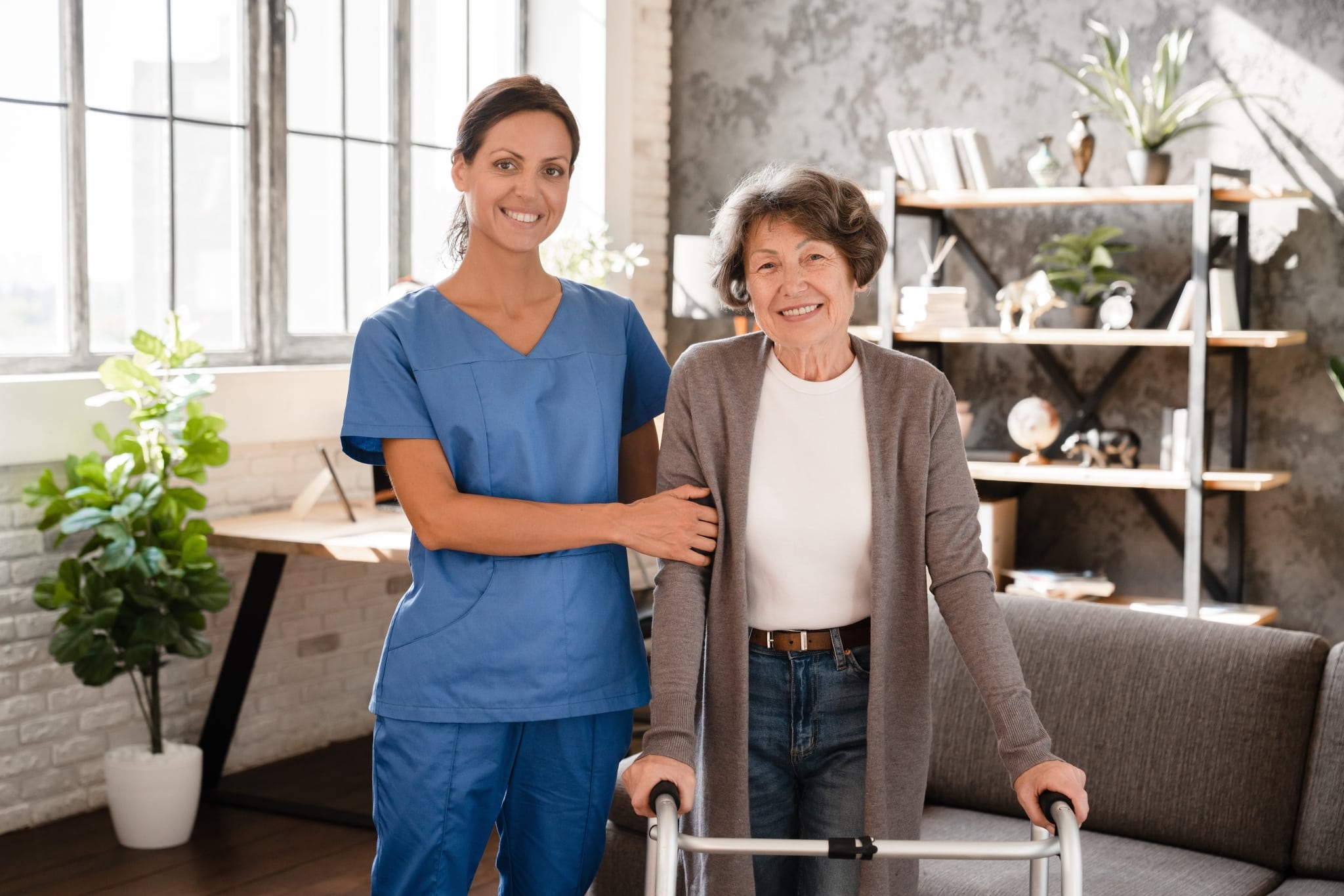 Female professional in scrubs helping an older woman use a walker
