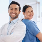 Two medical professionals smiling back to back with their arms crossed