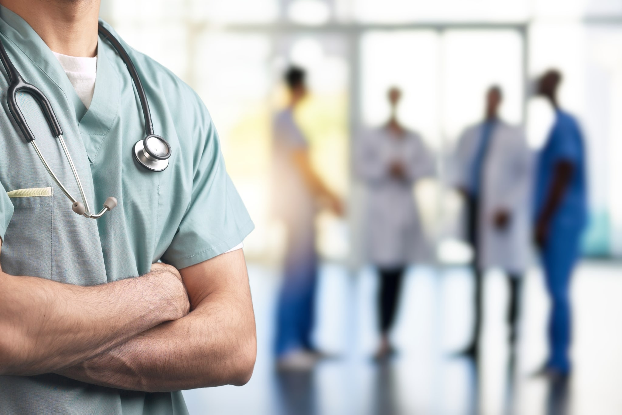 Close up of a man in scrubs with medical professionals behind him