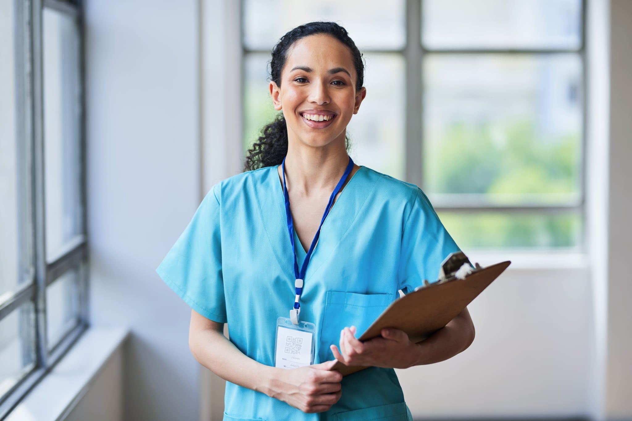 Smiling medical professional in scrubs holding a clipboard