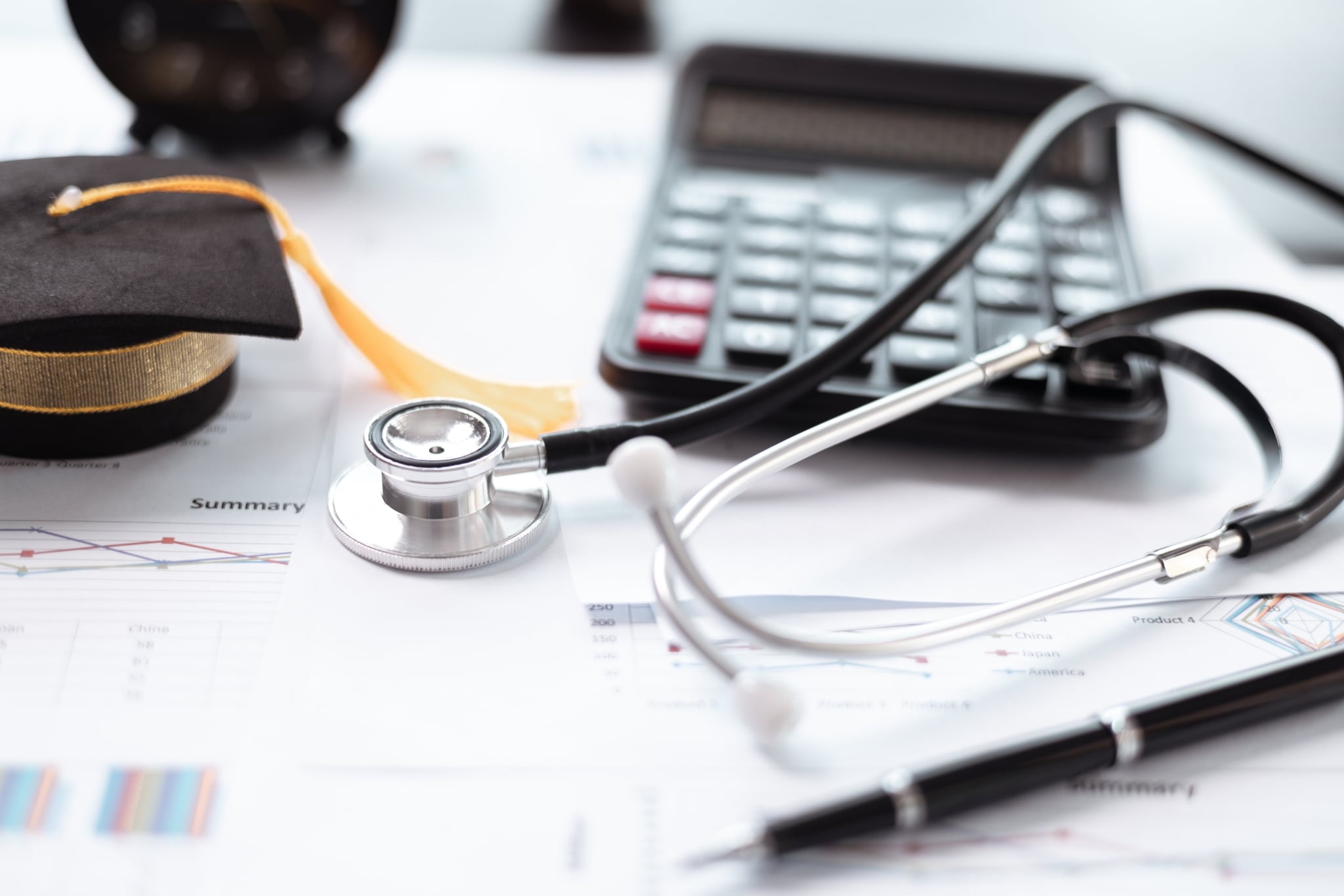 Close up of a calculator, stethoscope, and mini graduation cap