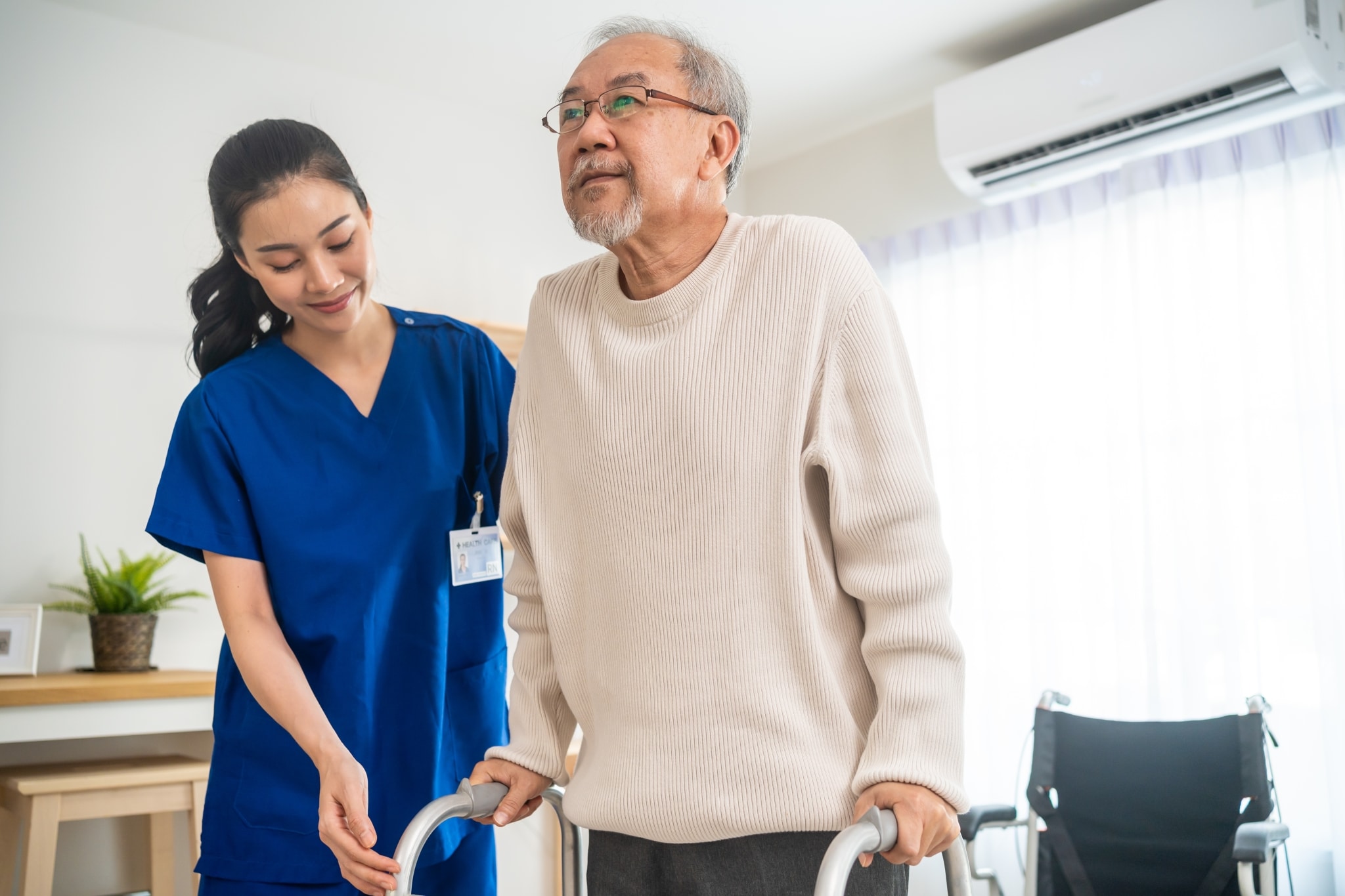 Asian medical professional helping an elderly man use a walker