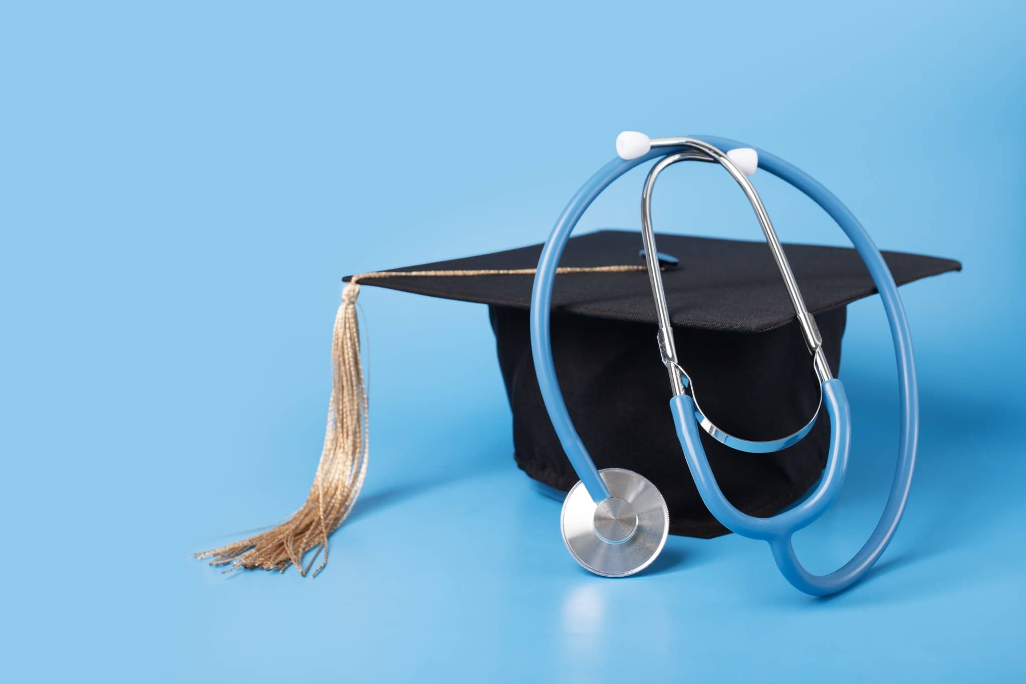 Graduation cap and stethoscope against a light blue backdrop